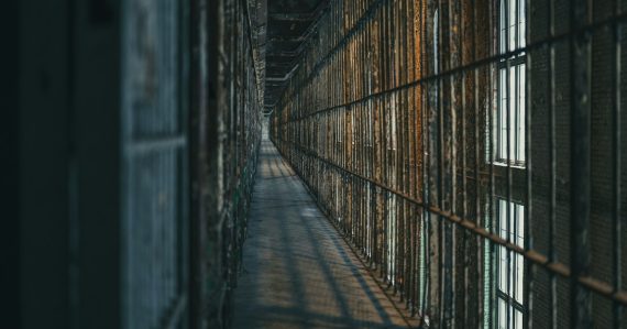Dimly lit prison corridor with barred cells, illustrating in-cell phones versus contraband cellphones
