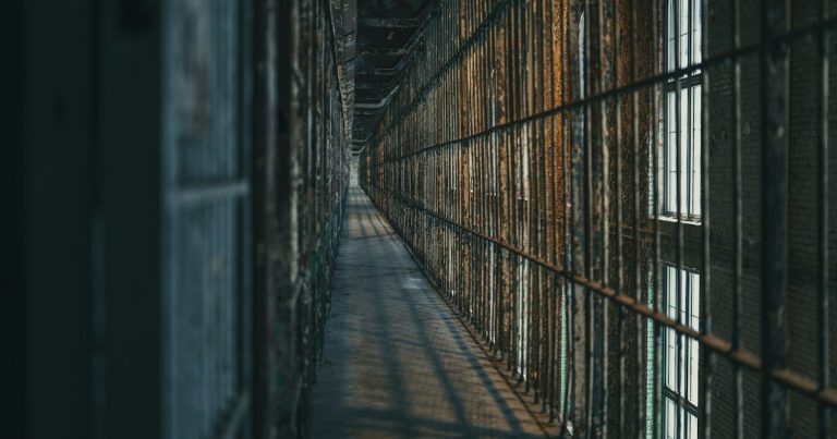 Dimly lit prison corridor with barred cells, illustrating in-cell phones versus contraband cellphones