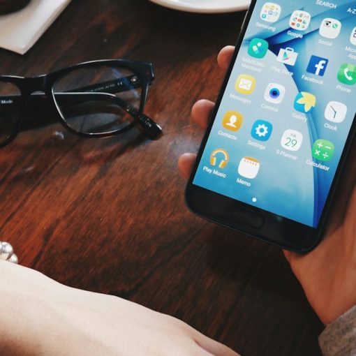Person holding a smartphone at a table with a cup and saucer, illustrating the FCC contraband device rulemaking