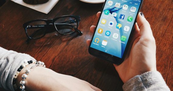 Person holding a smartphone at a table with a cup and saucer, illustrating the FCC contraband device rulemaking
