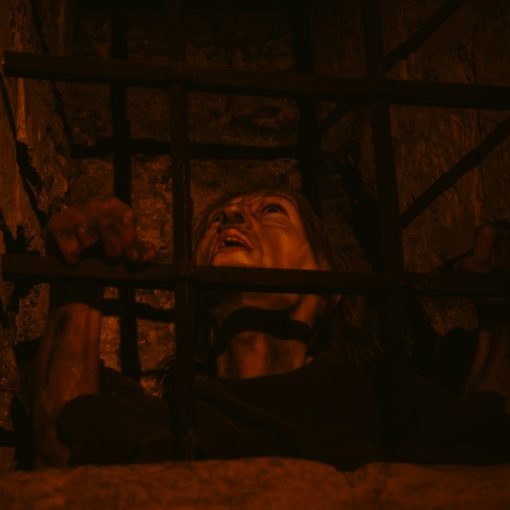 A person's face behind prison bars, illustrating an editorial against phones in cells