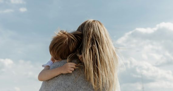 Woman holding child from behind against cloudy sky, illustrating a mother convicted of smuggling phones