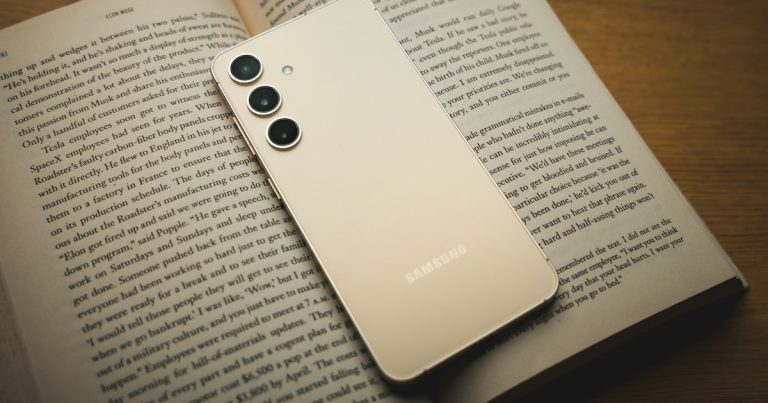 A white samsung phone sitting on top of an open book, illustrating the high value of contraband phones