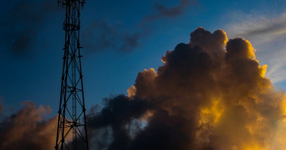 Cell tower silhouetted against a dramatic sunset sky, illustrating caution on prison managed access