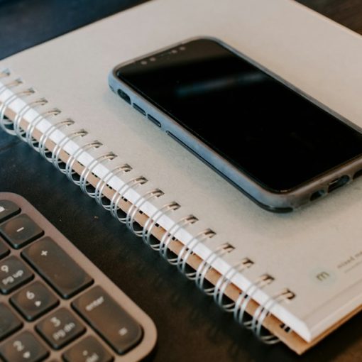 A cell phone sitting on top of a notebook next to a keyboard, illustrating mobility in corrections