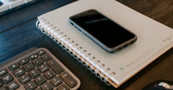 A cell phone sitting on top of a notebook next to a keyboard, illustrating mobility in corrections