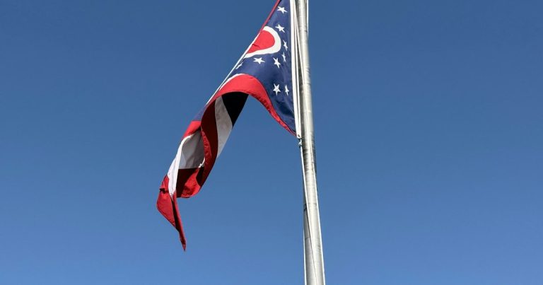Ohio state flag flying on a flagpole against blue sky, illustrating contraband phones in Ohio prisons