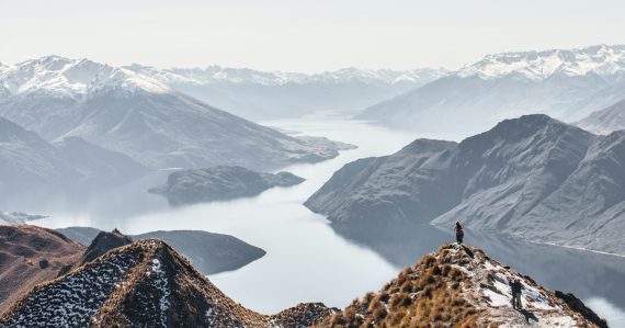 People on a rocky mountain peak overlooking a large lake and snowy mountains, illustrating in-cell phones at a new NZ prison