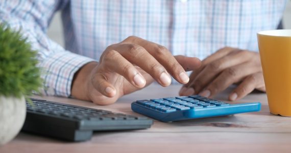 Person using calculator at desk with coffee mug, illustrating state prison budget pressures