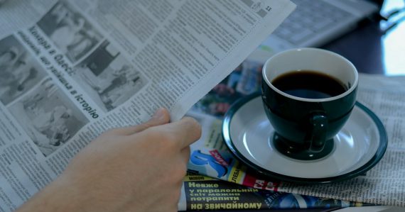 A person reading a newspaper with a cup of coffee, illustrating a roundup of contraband phone news