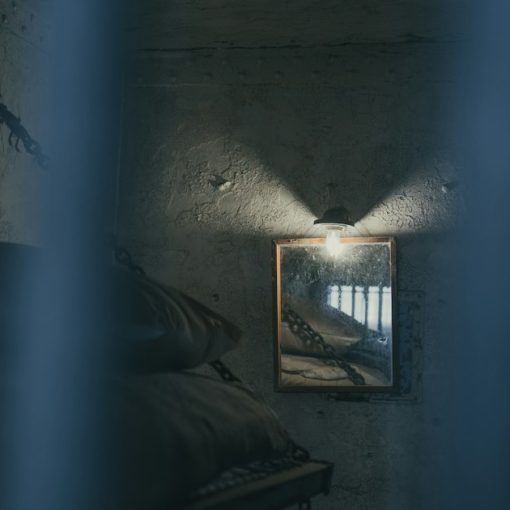 Dimly lit prison cell with a bed and barred window, illustrating the dual nature of prison cellphones