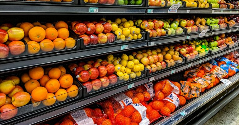 Shelves of fresh oranges, apples, lemons, and limes in a grocery store, illustrating cell phones as a commissary item