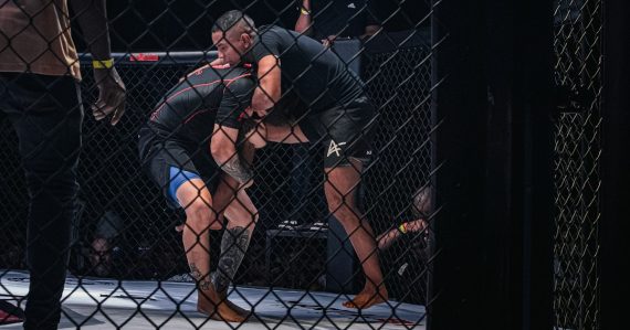 Two fighters grappling inside a cage, illustrating a prison fight blamed on phones
