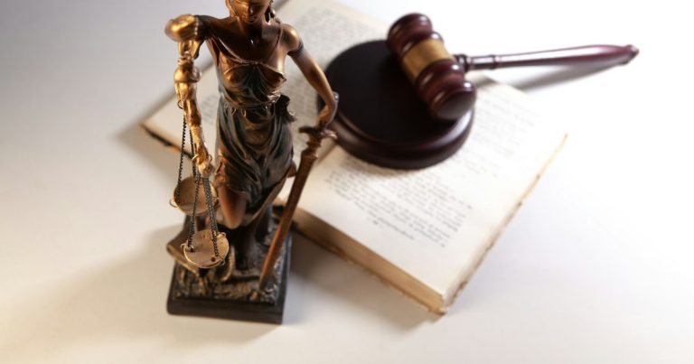 Statue of justice, gavel, and open book on table, illustrating a guard facing trial for smuggling