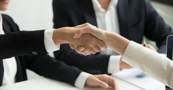Two people shaking hands in front of a laptop, illustrating prison payphone industry consolidation