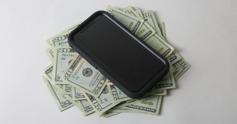 A cell phone sitting on top of a pile of money, illustrating prison phone price gouging