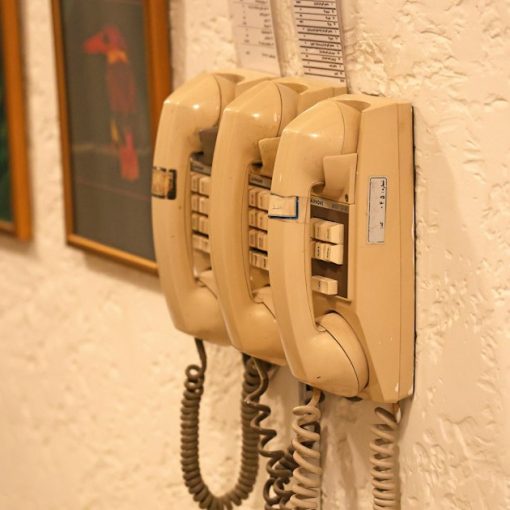 Three beige wall-mounted telephones with coiled cords, illustrating phones in cells aiding rehabilitation