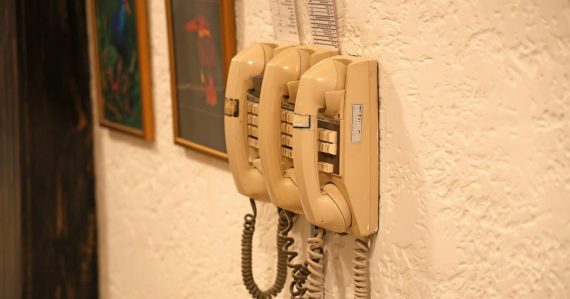 Three beige wall-mounted telephones with coiled cords, illustrating phones in cells aiding rehabilitation