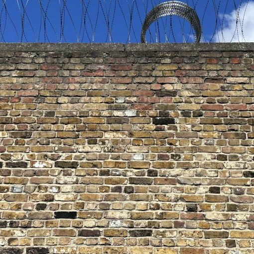 A brick wall with barbed wire on top of it, illustrating contraband in regional jails