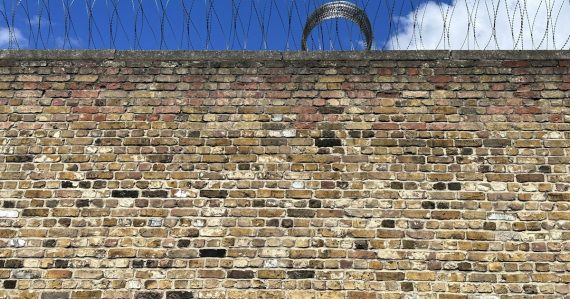 A brick wall with barbed wire on top of it, illustrating contraband in regional jails