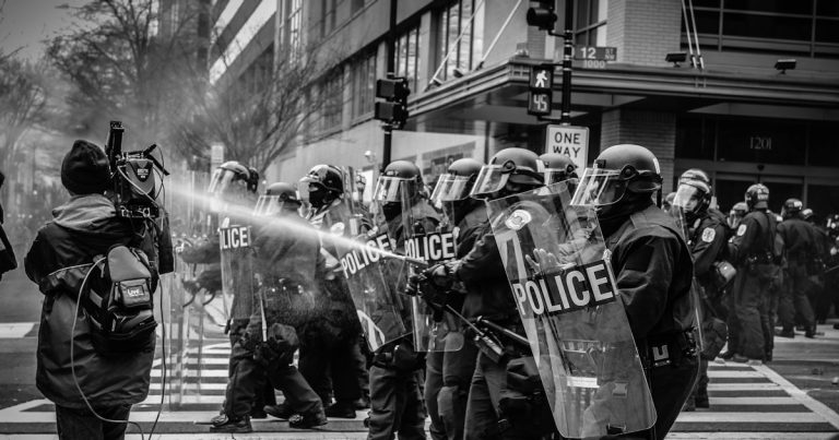 Grayscale photo of police riot team on pedestrian lane, illustrating a riot over confiscated phones
