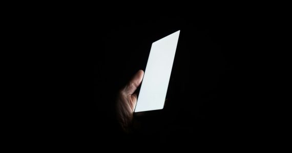 Person holding smartphone at night, illustrating contraband phones as a dangerous weapon