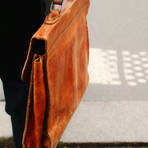 A person holding a brown briefcase on a sidewalk, illustrating a lawyer smuggling phones in shoes