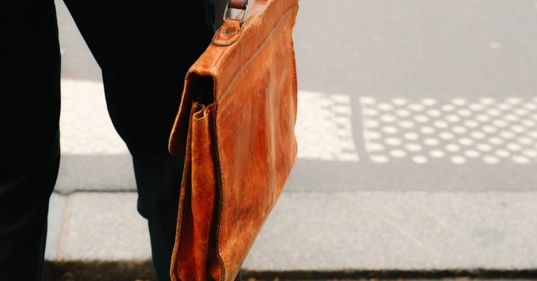 A person holding a brown briefcase on a sidewalk, illustrating a lawyer smuggling phones in shoes