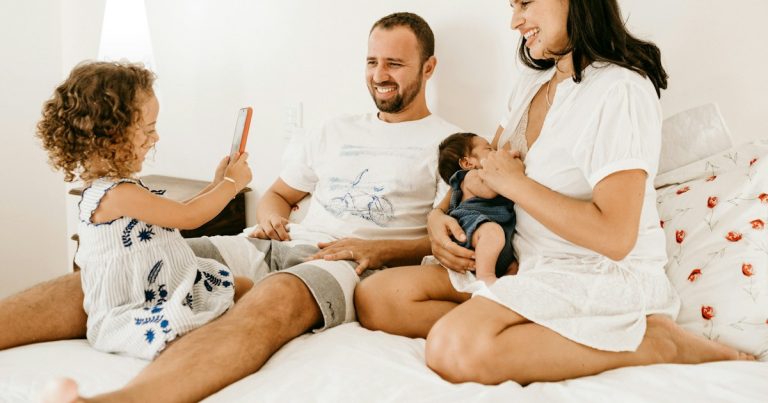 A family on a bed, a child holding a phone, an adult holding a baby, illustrating the challenges of jail visits